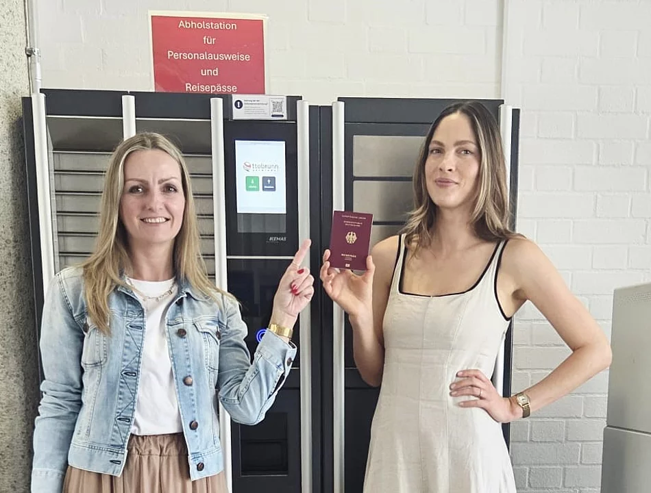 Nutzen auch Sie die Box im Eingangsbereich, um Ihren Personalausweis oder Reisepass abzuholen. Zwei Rathausmitarbeiterinnen stehen vor der Abholstation